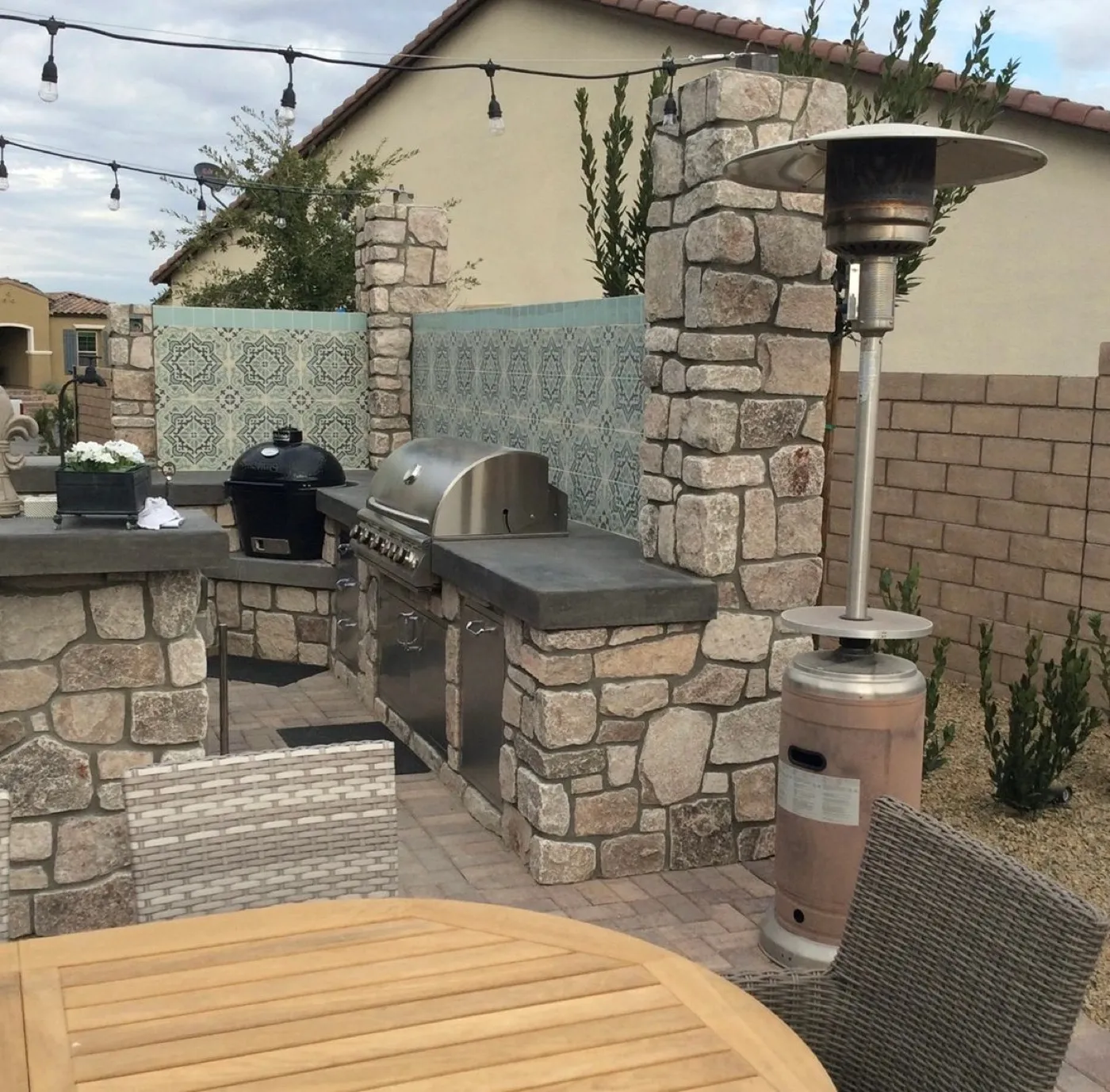Stone veneer outdoor kitchen with a built-in grill, kamado grill and gray concrete counters on a paver patio