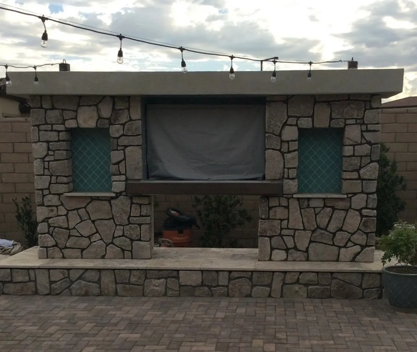 Outdoor stone veneer fireplace and media wall built in a Las Vegas backyard, with the fireplace opening below a covered television niche