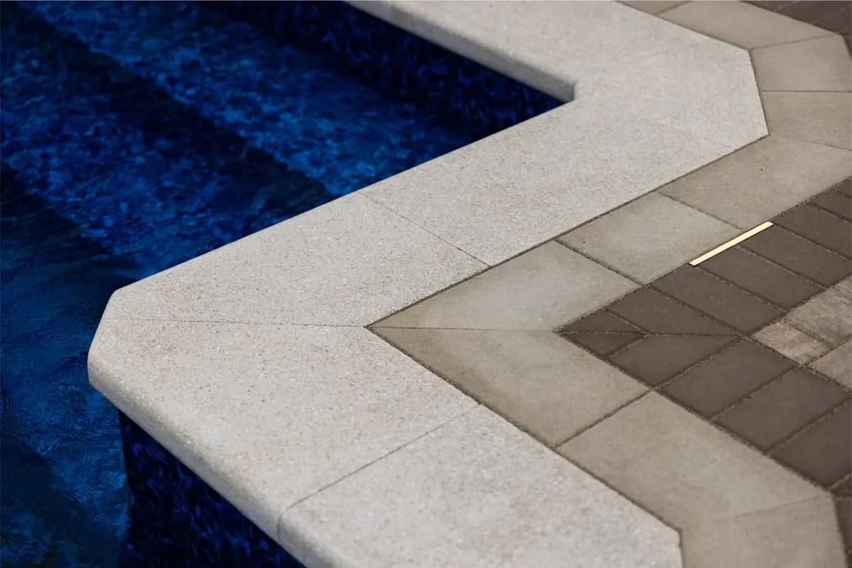 Bullnose pool coping turning a corner beside a two-tone paver border