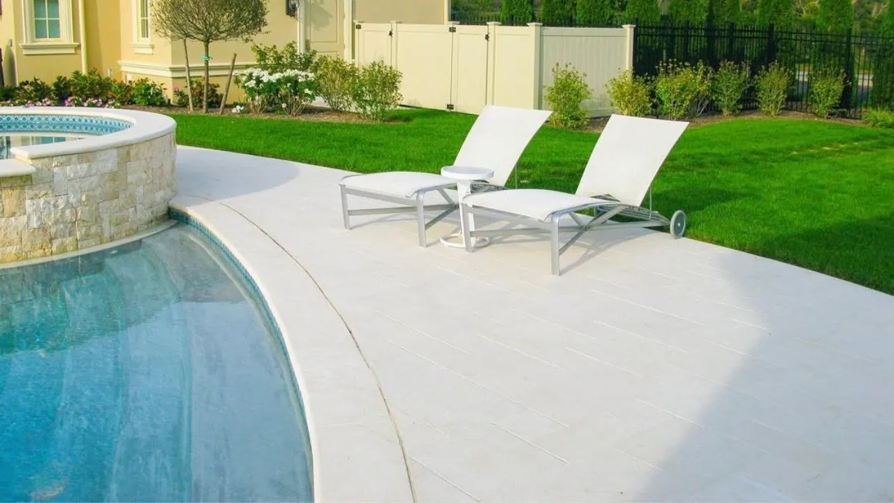 Light-colored pool deck with rounded coping along the water, a raised stacked-stone spa and two lounge chairs