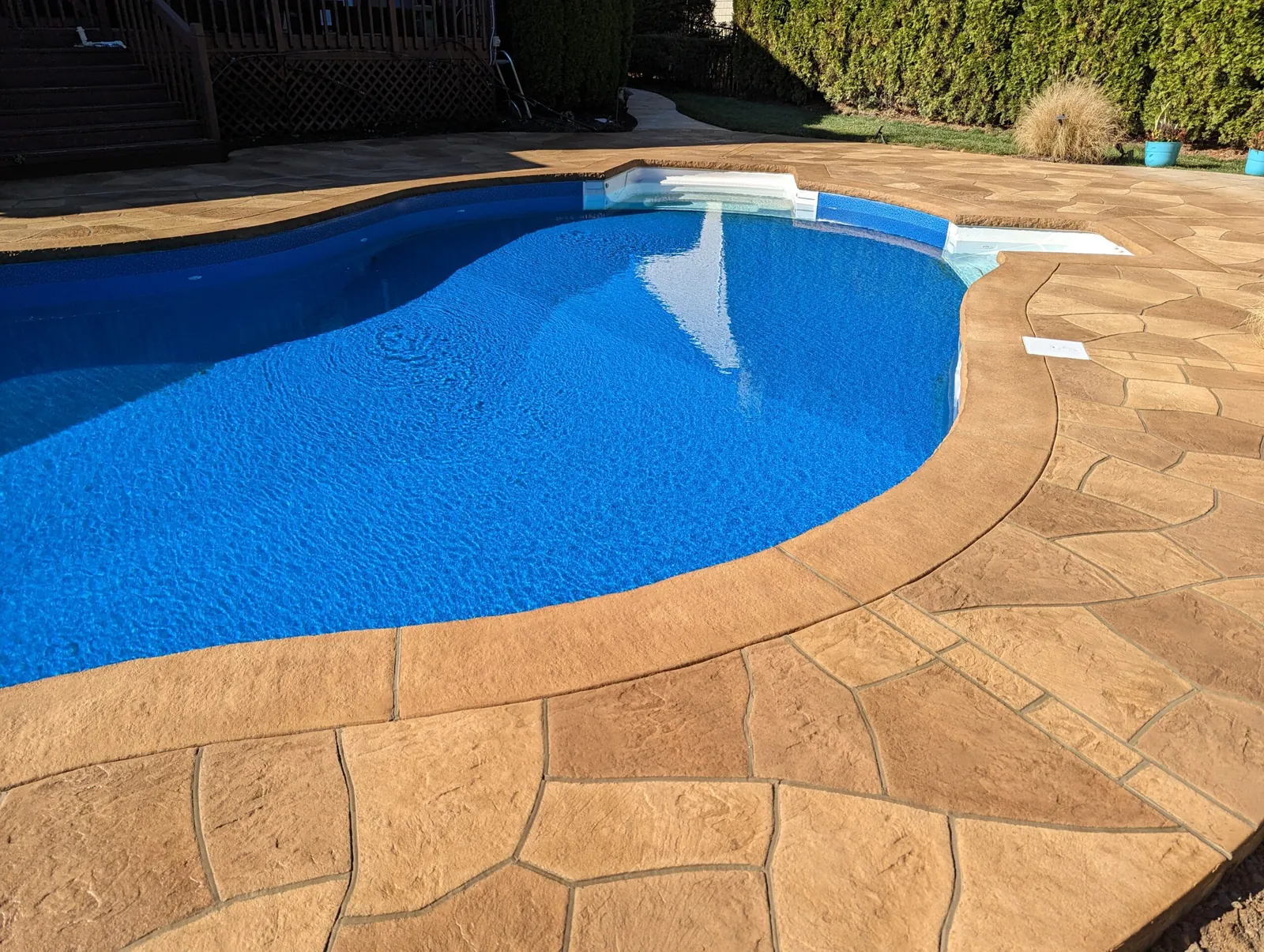 Stamped concrete pool deck in a flagstone pattern curving around a pool